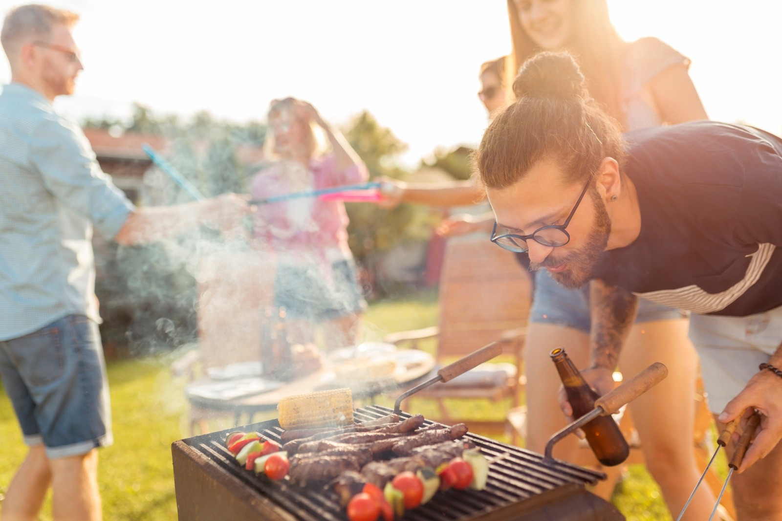 Man preparing food on an outdoor grill while spending time with family and friends.