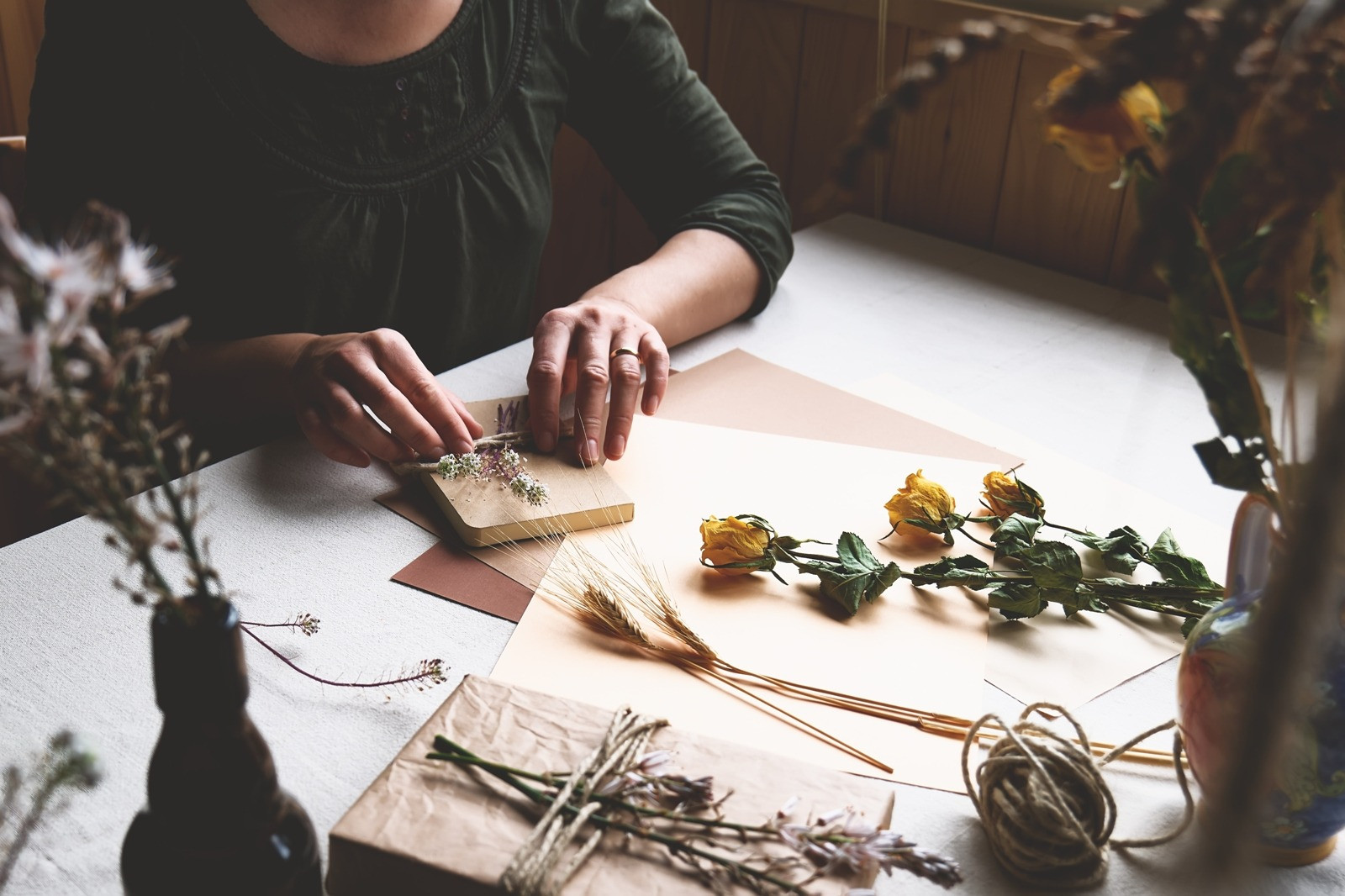 Person arranging dried flowers and natural materials on a table, creating a calm, mindful atmosphere for rest and reflection.