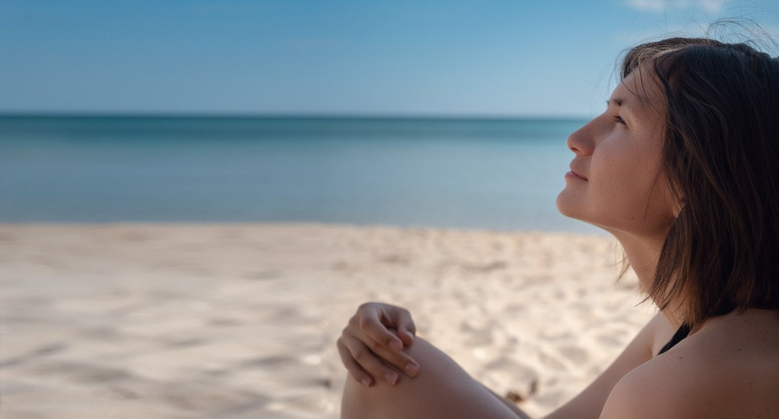 Woman sitting peacefully by the beach with her eyes closed