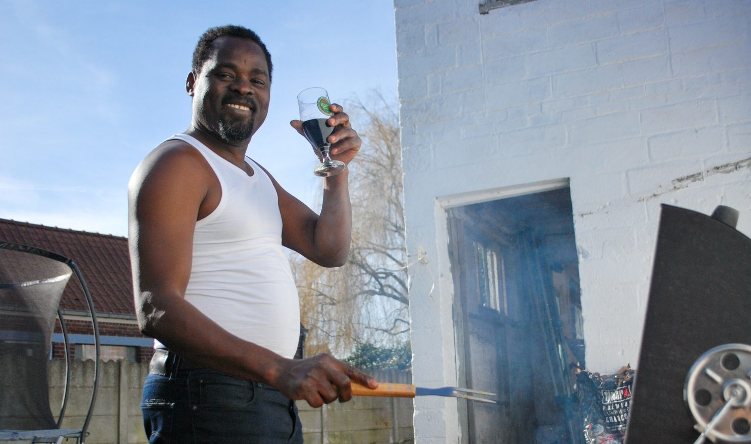 Man standing outdoors by a barbecue grill while holding a drink