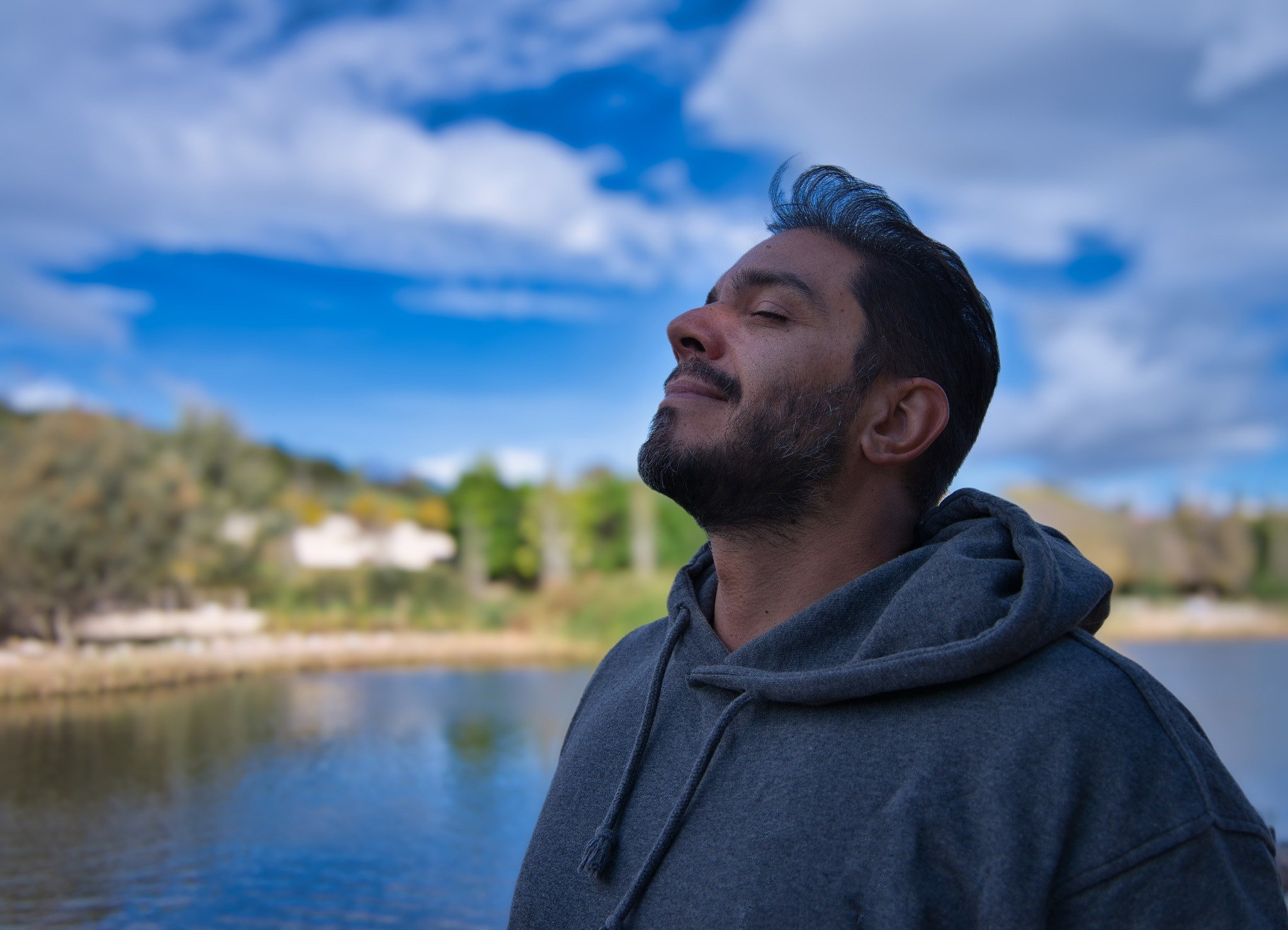Man standing outdoors by a lake with his eyes closed