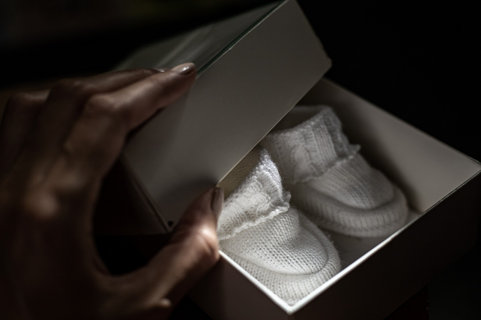 Close-up of hands opening a box containing white knitted baby booties.