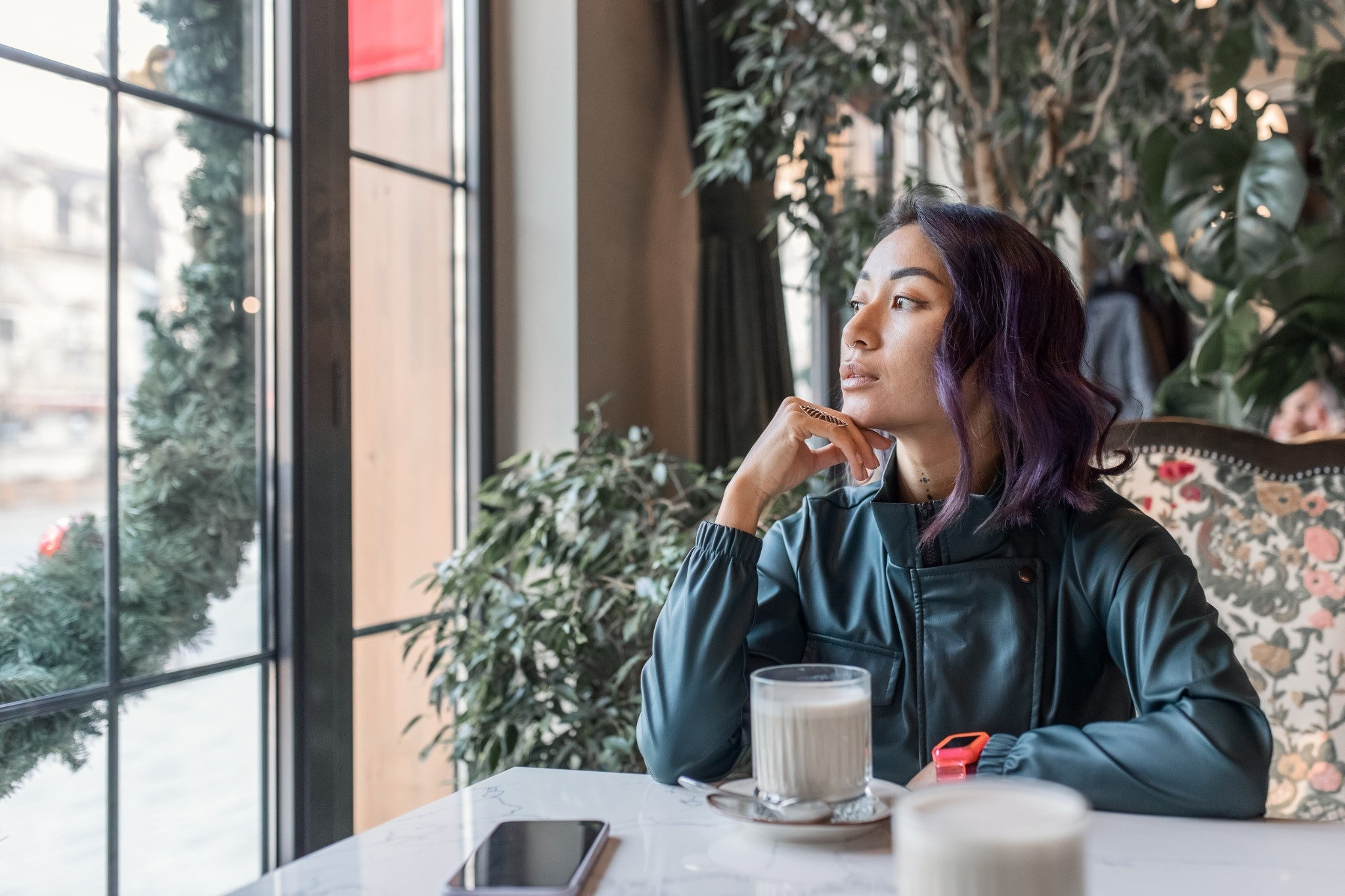 Woman sitting by a window with a drink and looking outside thoughtfully