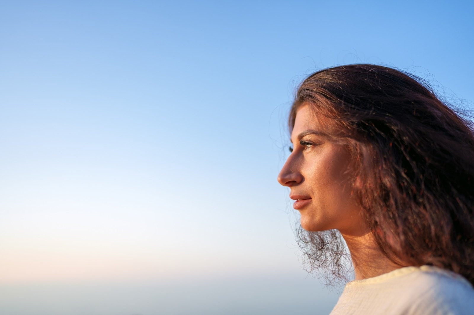 Woman with long brown hair looking into the distance against a clear blue sky.
