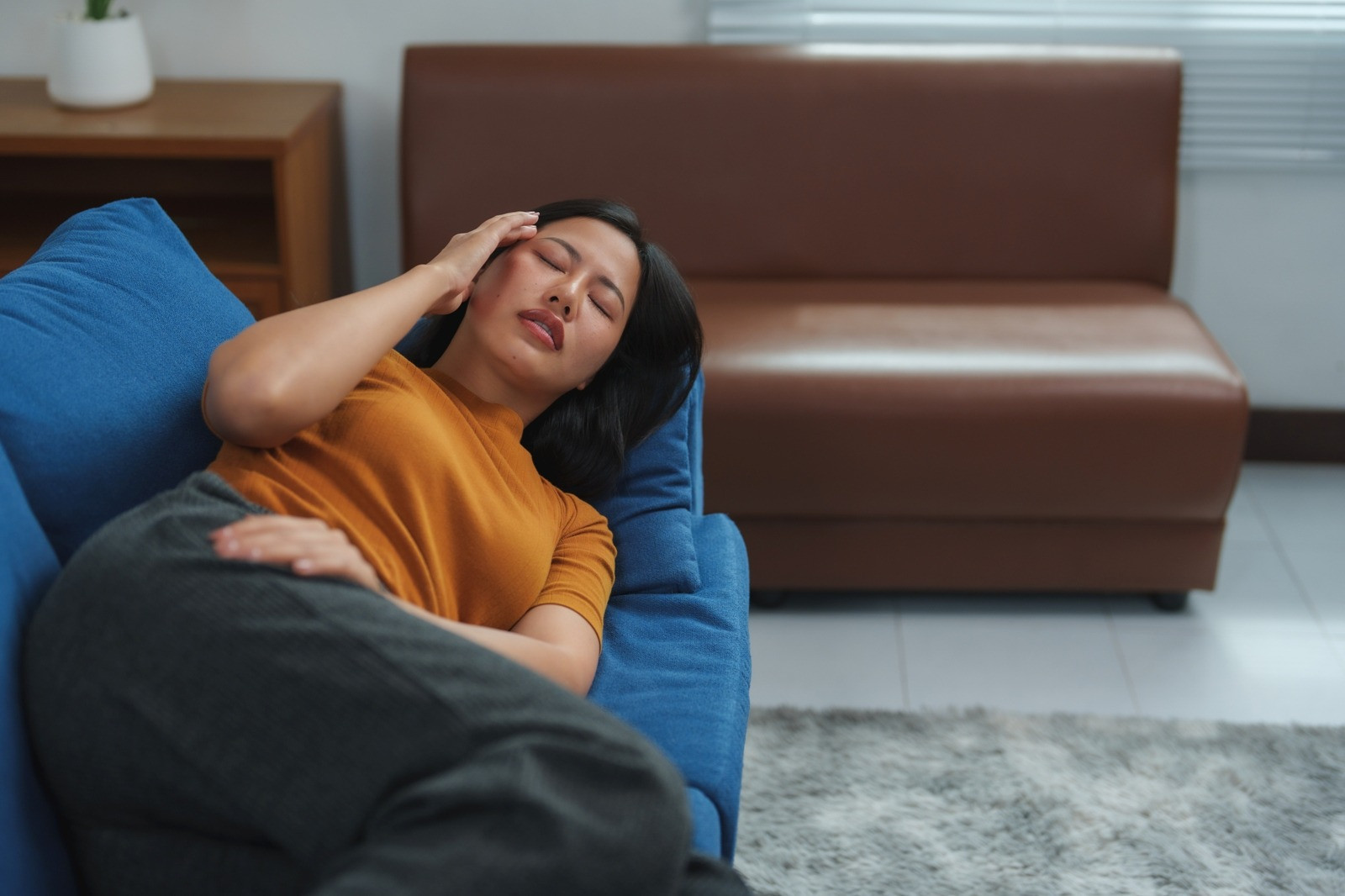 Woman resting with her eyes closed on a couch in a quiet indoor setting.