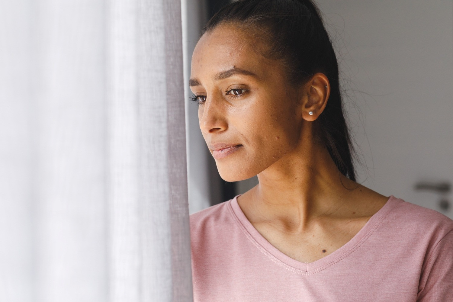 Woman standing beside a bright window and looking outside thoughtfully after an EMDR session.