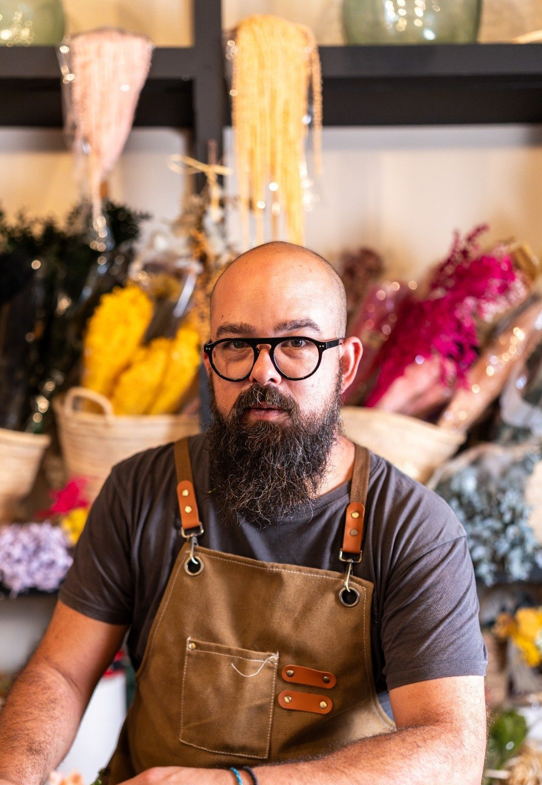 Bearded man wearing an apron arranging flowers at a worktable