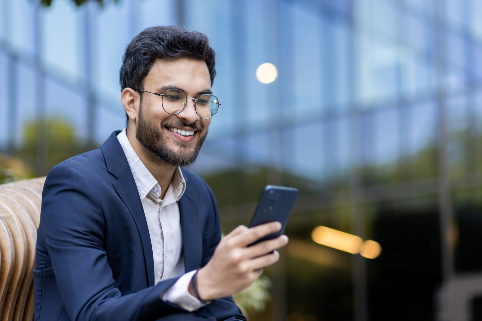 Smiling man holding a smartphone while seated outdoors, representing a self-guided EMDR option that may include tapping instead of eye movements.