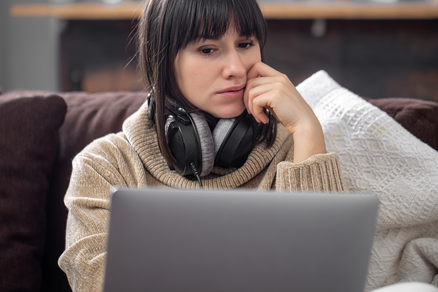 Woman sitting on a couch with headphones around her neck, looking thoughtfully at a laptop after an EMDR session.