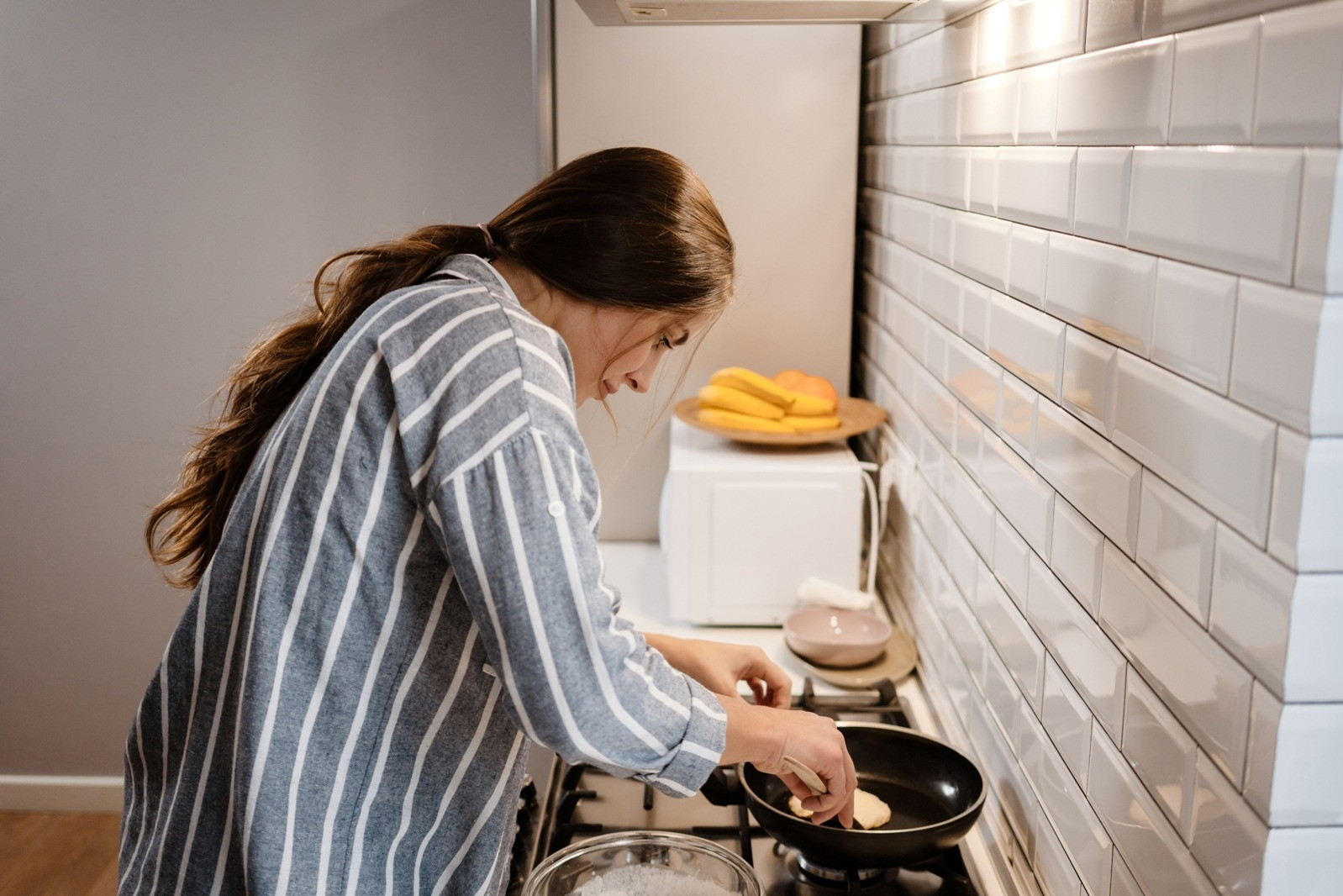 Woman cooking at a stovetop in a bright home kitchen.