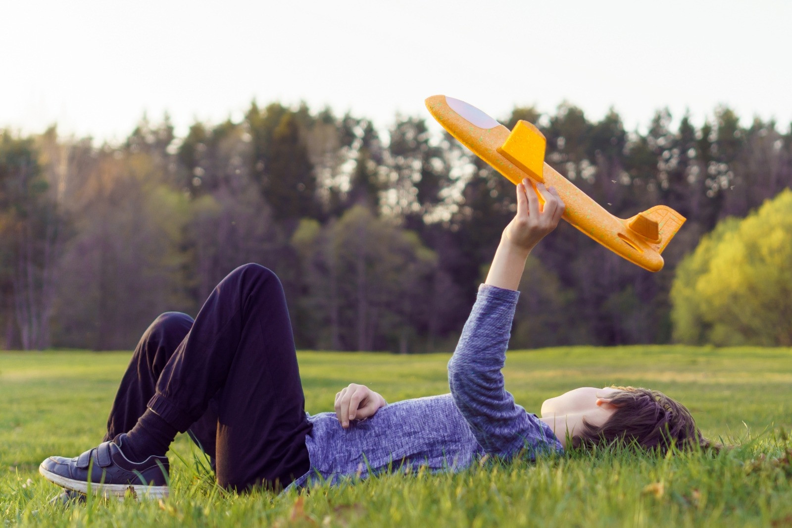 Child lying on grass while holding a toy airplane in the air