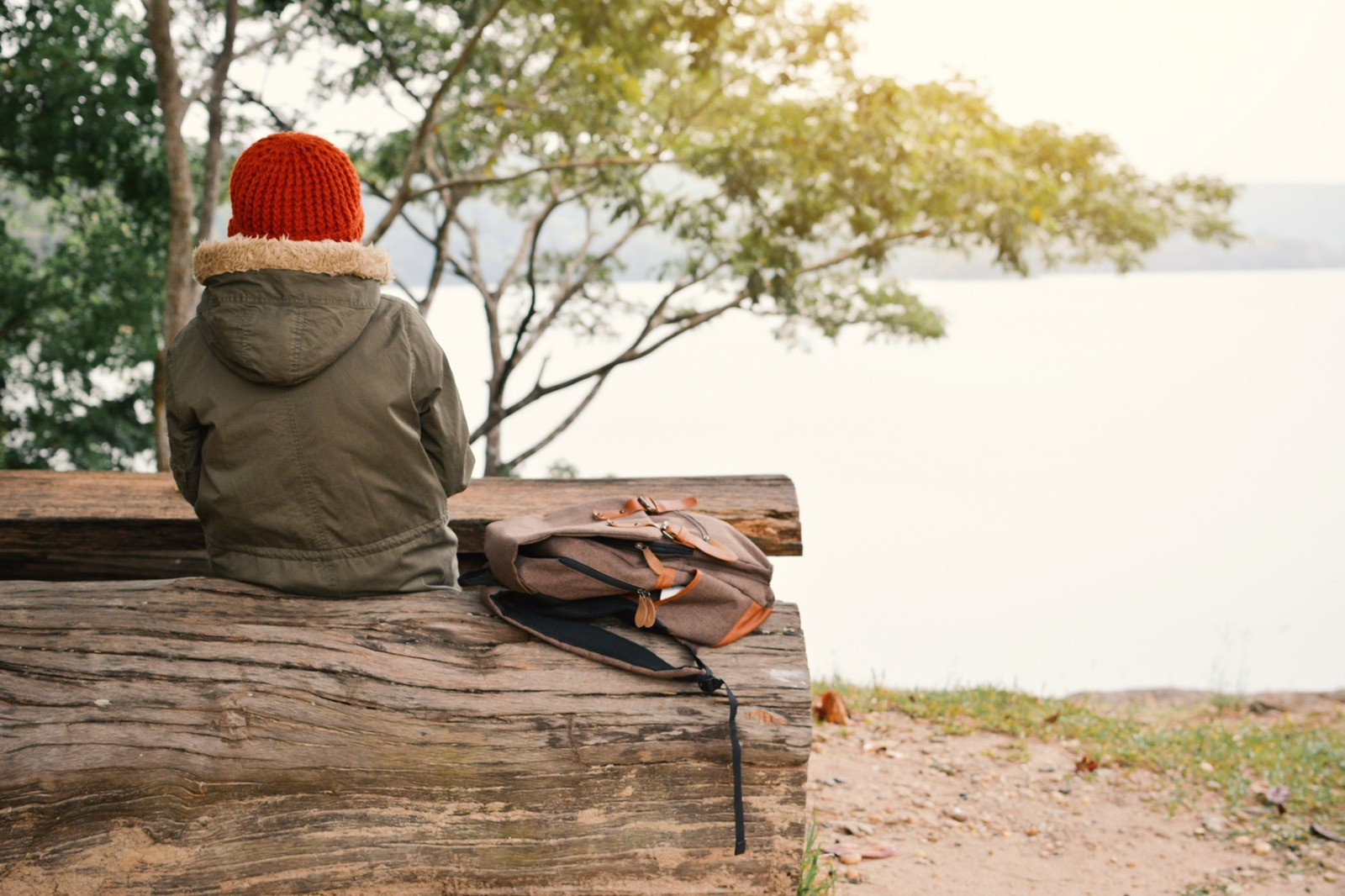 Person sitting on a wooden bench by a calm lake, looking out at the water in a quiet outdoor setting.