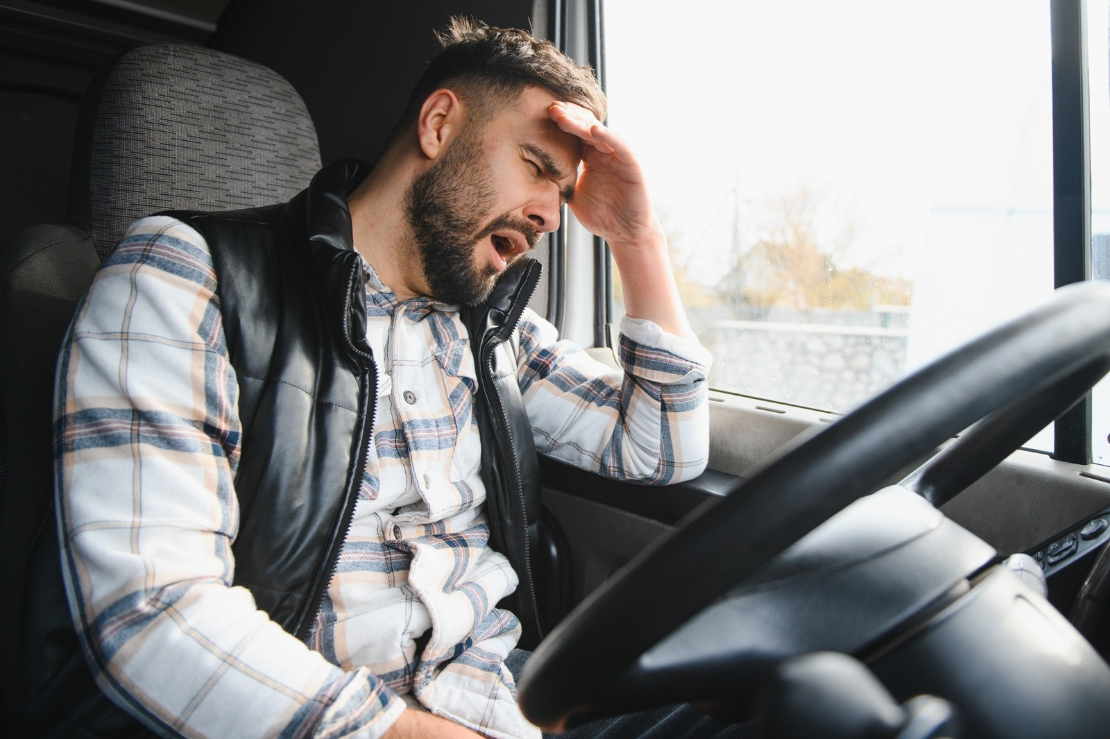 Tired man sitting in a vehicle with his hand on his forehead, illustrating fatigue during or after an EMDR session.