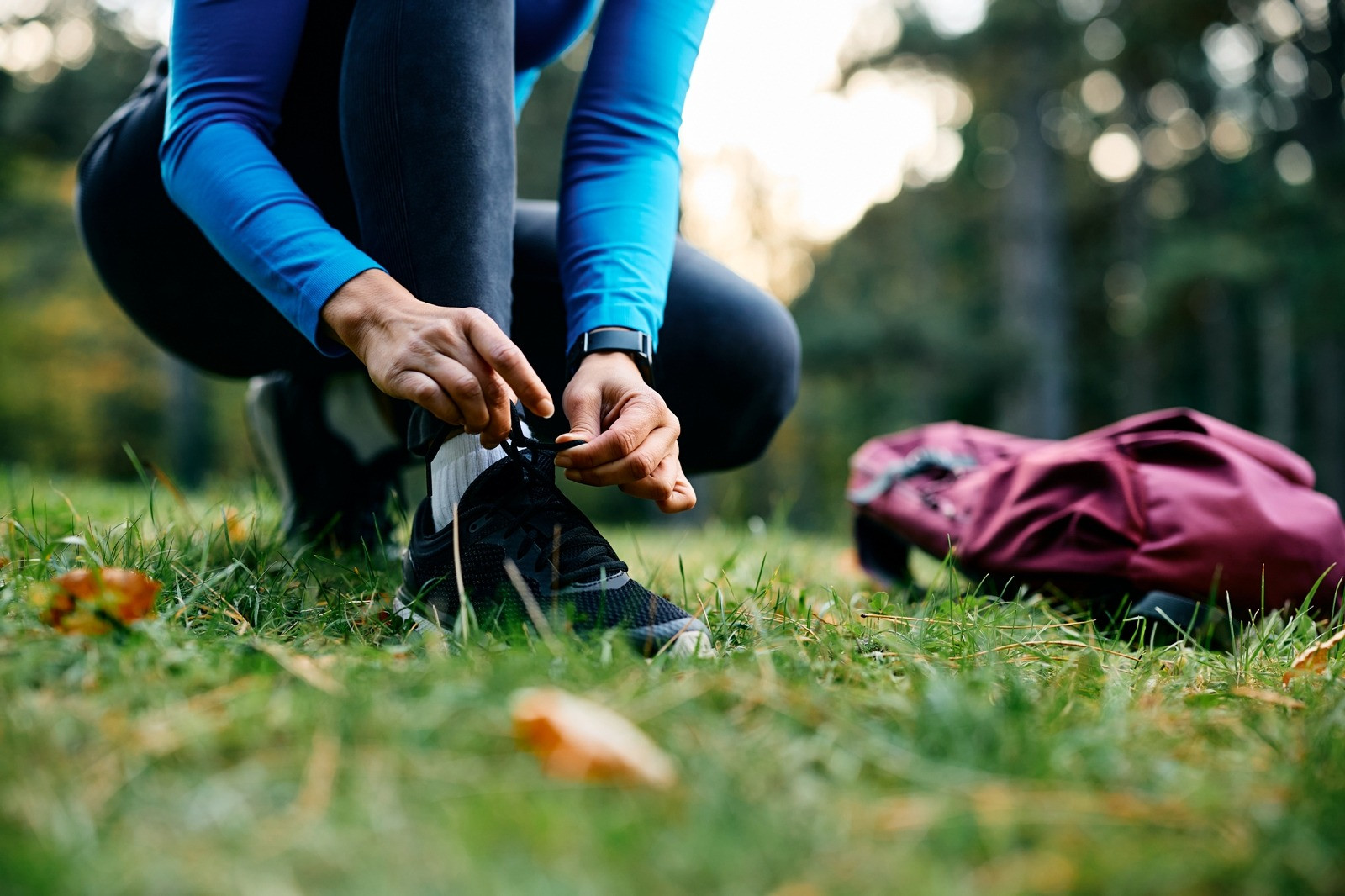 Person tying their running shoes outdoors before exercise, with a sports bag resting nearby.