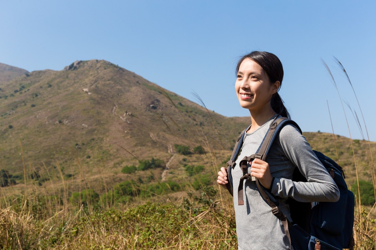 Woman wearing a backpack while walking outdoors in a sunny mountain landscape