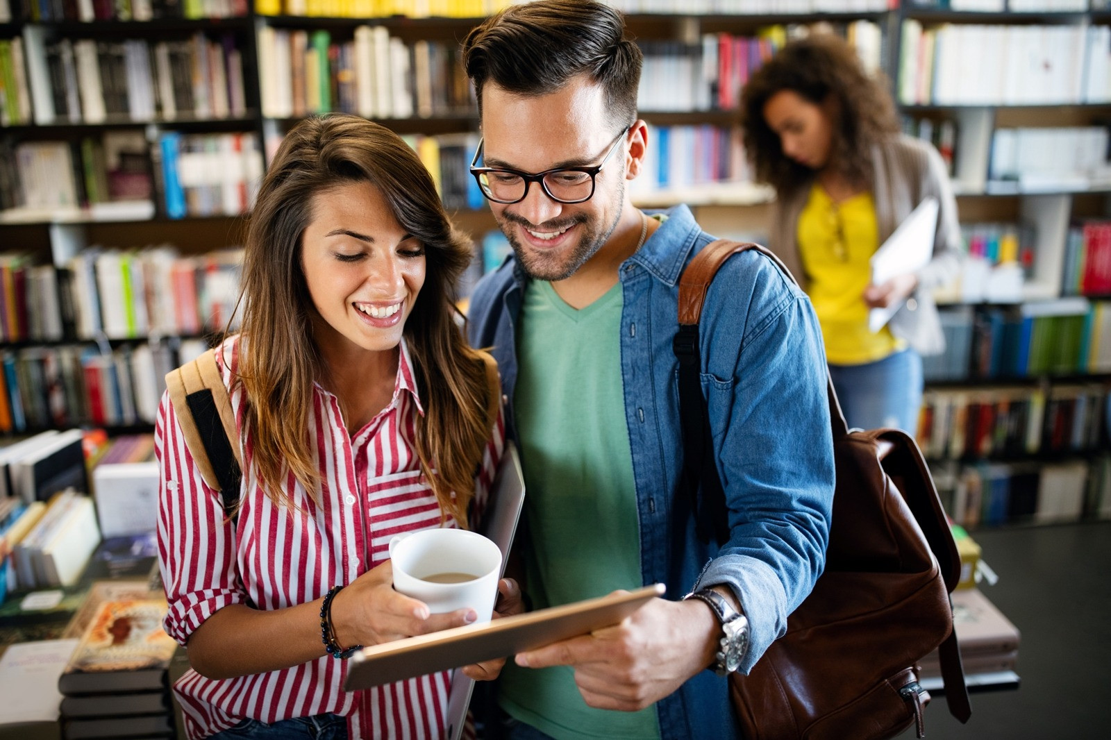 Smiling man and woman looking at a tablet together in a library, reflecting a calm and positive experience.