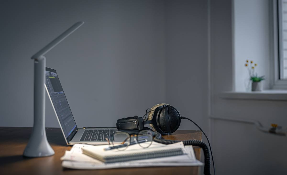 Laptop, headphones, and notebook arranged on a desk for an at-home session