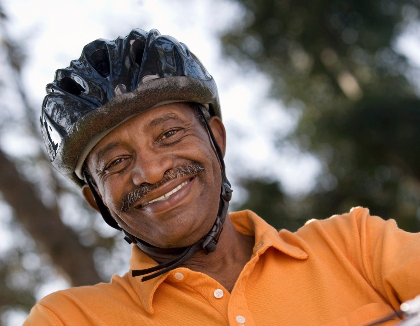 Smiling man wearing a bicycle helmet while riding a bike outdoors