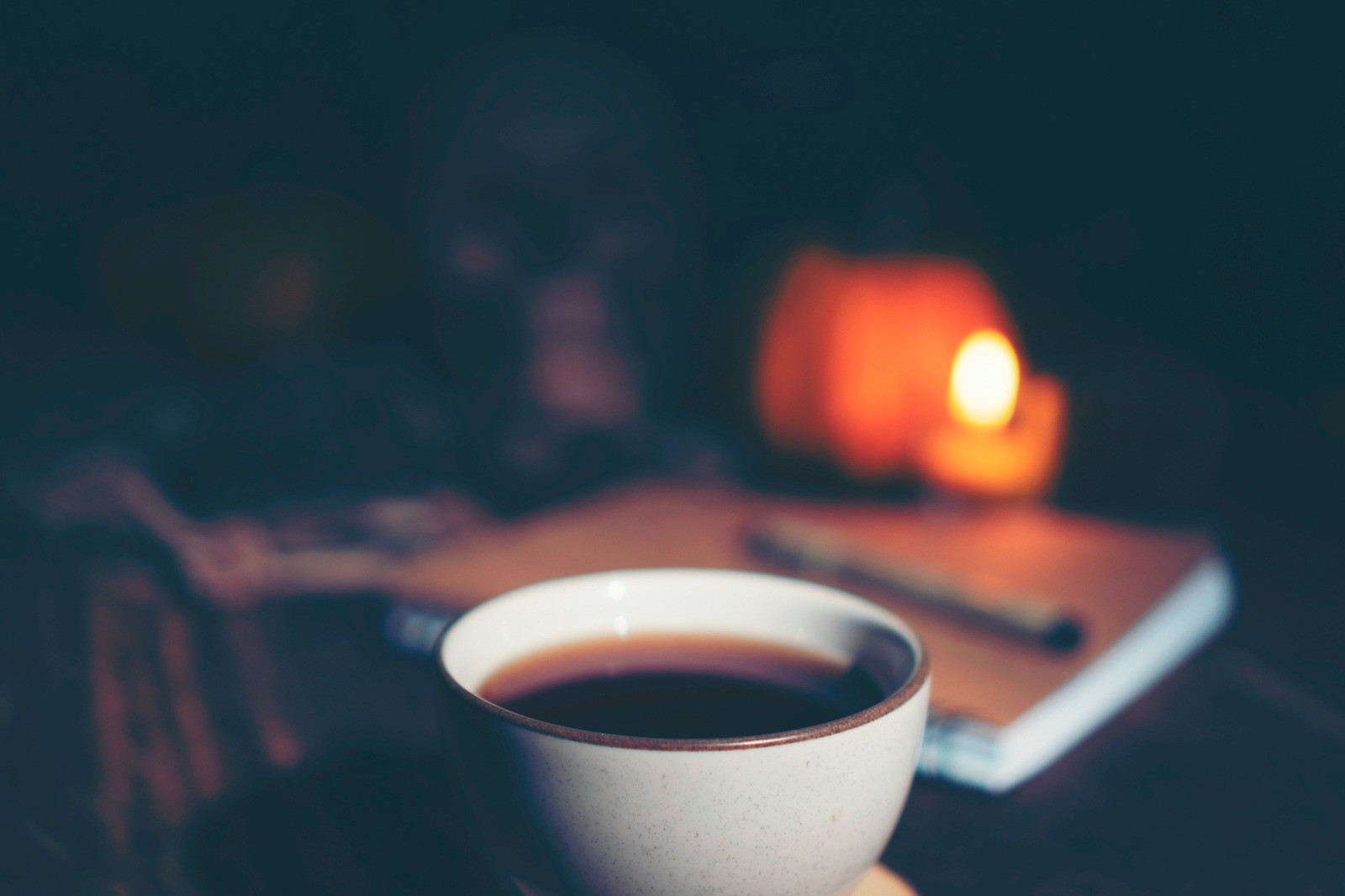 Cup of coffee beside headphones and a notebook in a softly lit room.