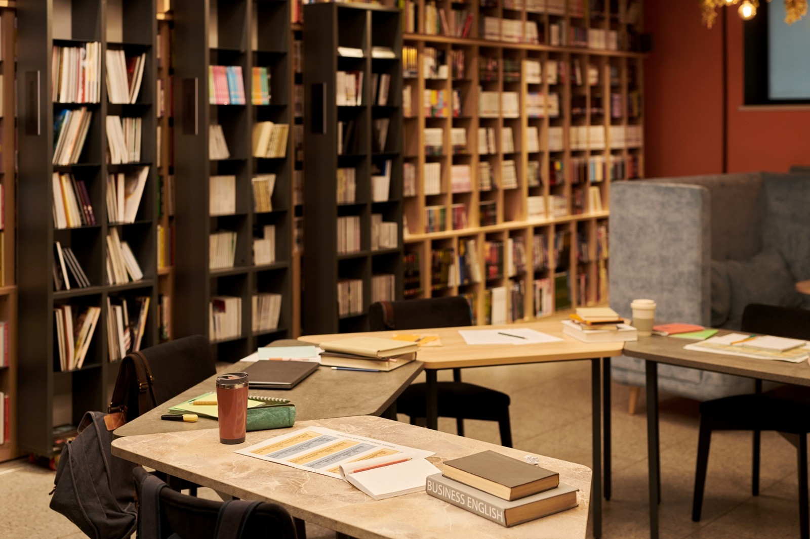 Warm, cozy library study space with bookshelves, wooden tables, notebooks, and writing materials arranged for quiet reflection and focused learning.