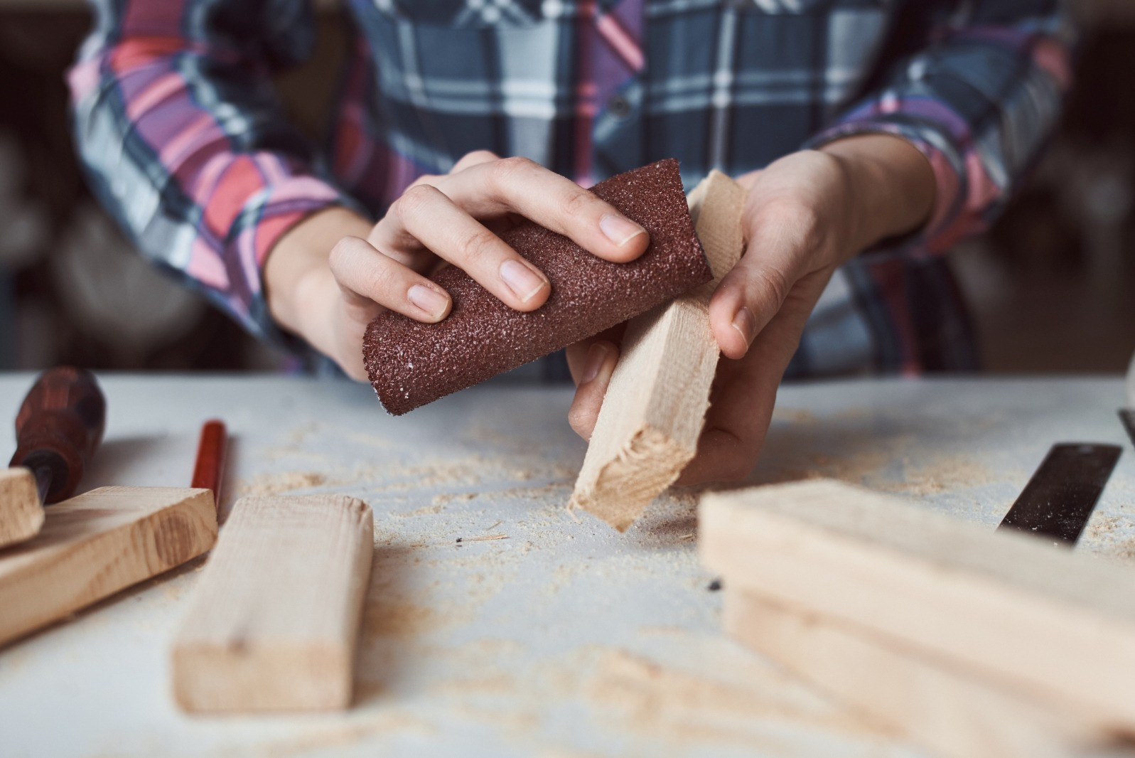 Close-up of a person sanding a wooden piece by hand at a workbench, illustrating a step-by-step process.