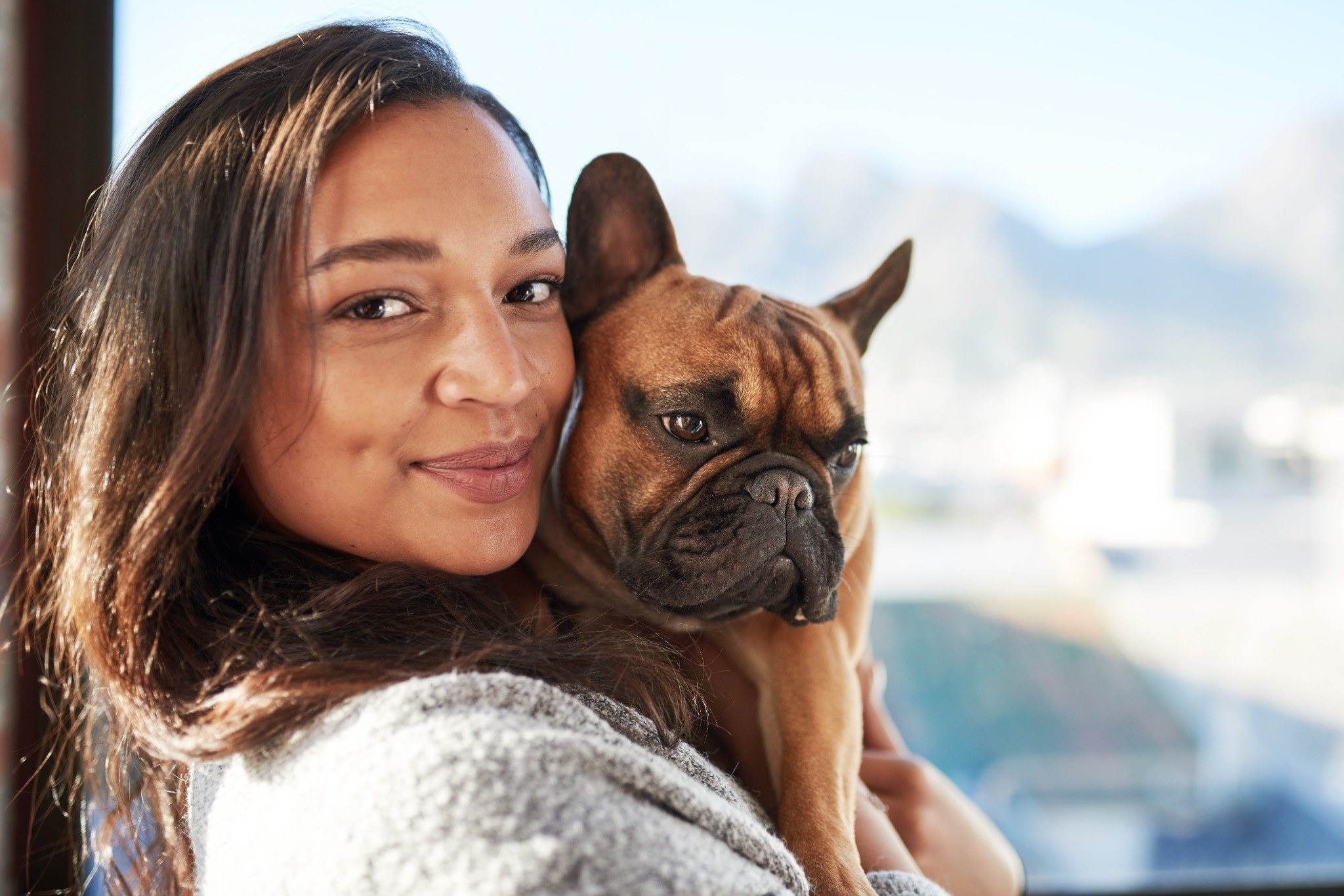 Woman holding a small dog near a bright window